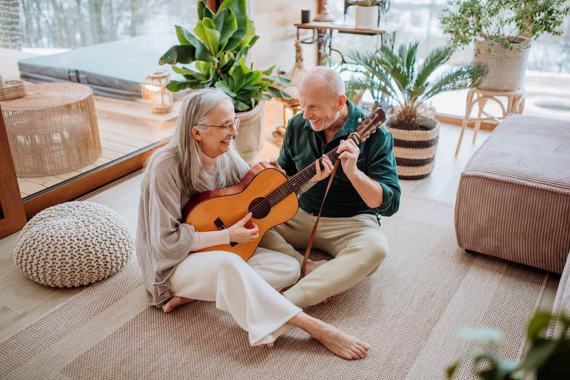 Eldre dame og mann sitter på gulvet hjemme og spiller gitar.